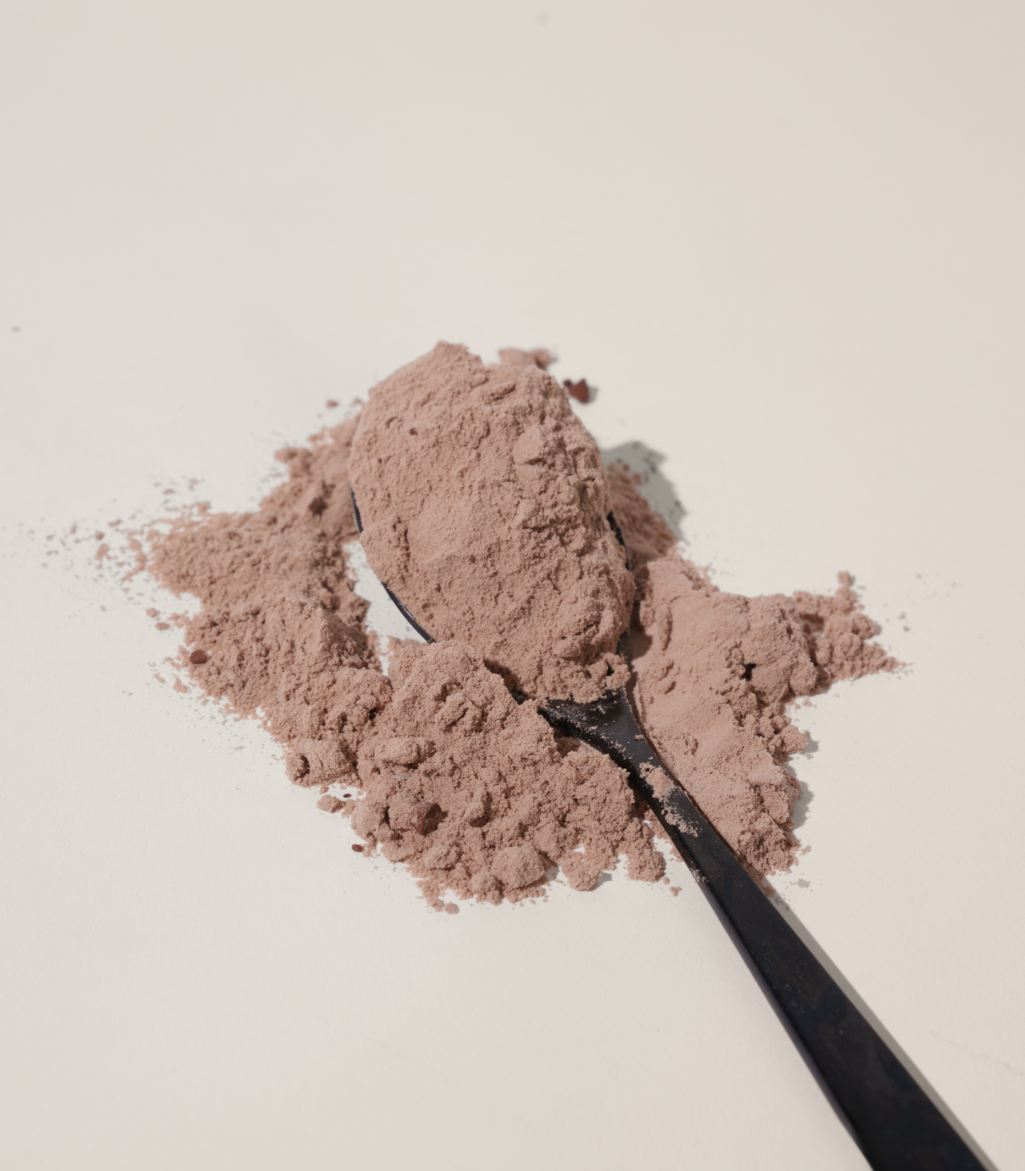 Grass-Fed Whey Protein powder on a black spoon against a light background.